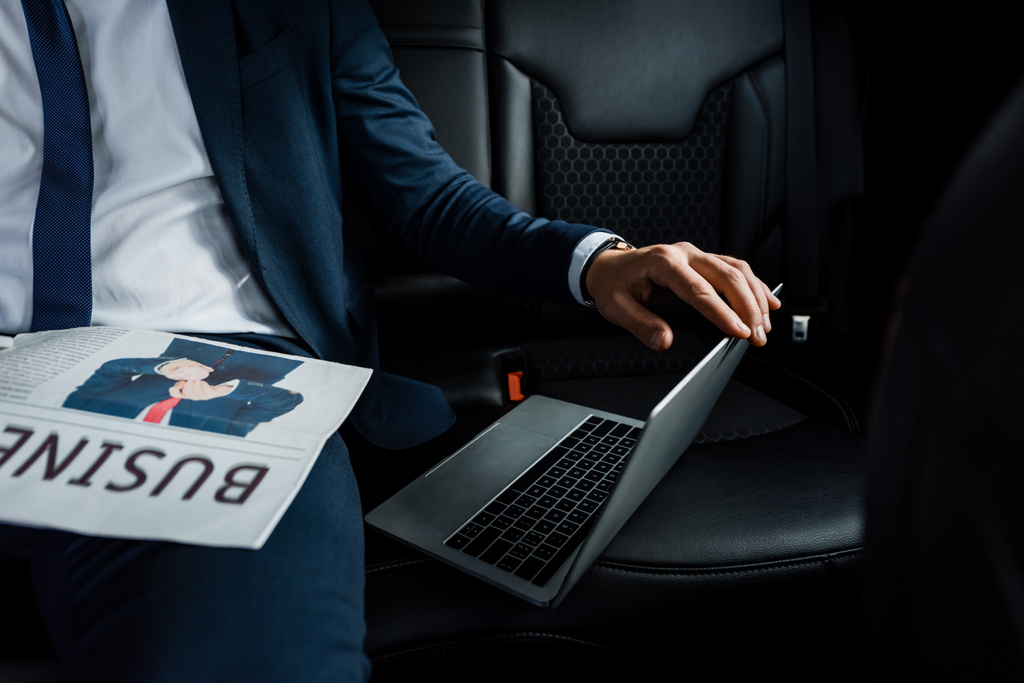 車の後部座席に新聞近くのノートパソコンに触れるビジネスマンの作物ビュー - 写真・画像