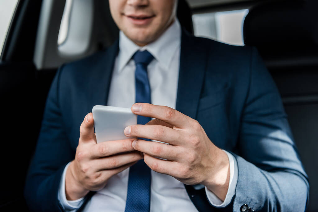 自動車の背景にぼやけているビジネスマンの手にスマートフォンの作物ビュー - 写真・画像