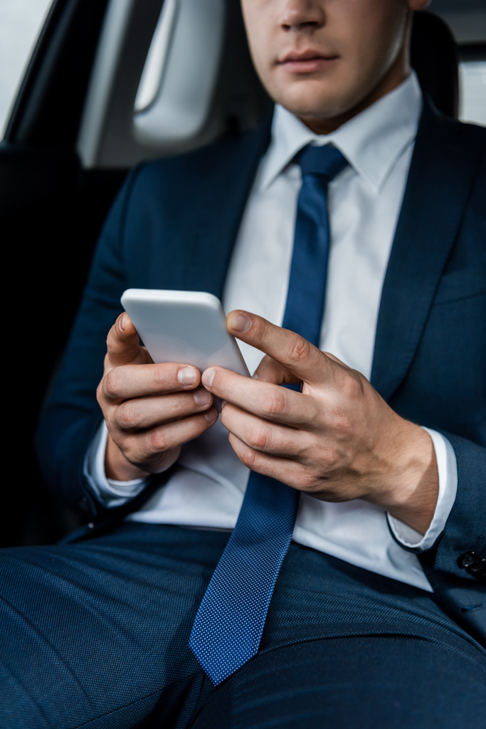 Обрезанный вид смартфона в руках молодого бизнесмена на размытом фоне в машине - Фото, изображение