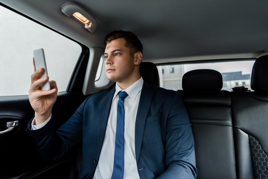 Mladý podnikatel v obleku pomocí mobilu v autě - Fotografie, Obrázek