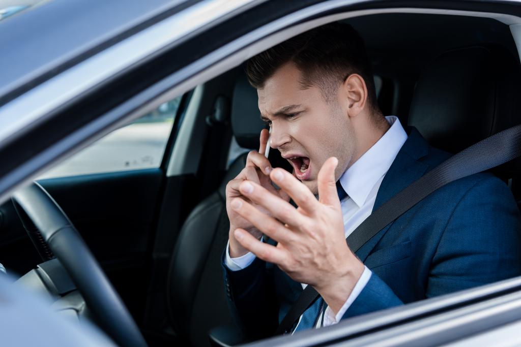 Angry businessman talking on smartphone in car on blurred foreground - Photo, Image