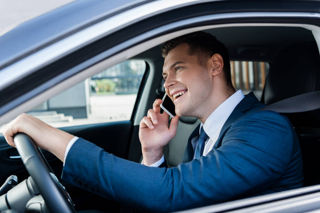 Mosolygó üzletember beszél okostelefonon vezetés közben autó elmosódott előtérben - Fotó, kép