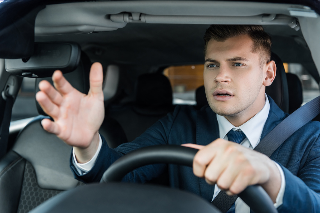 Biznesmen wskazując ręką podczas jazdy samochodem na niewyraźnym pierwszym planie - Zdjęcie, obraz