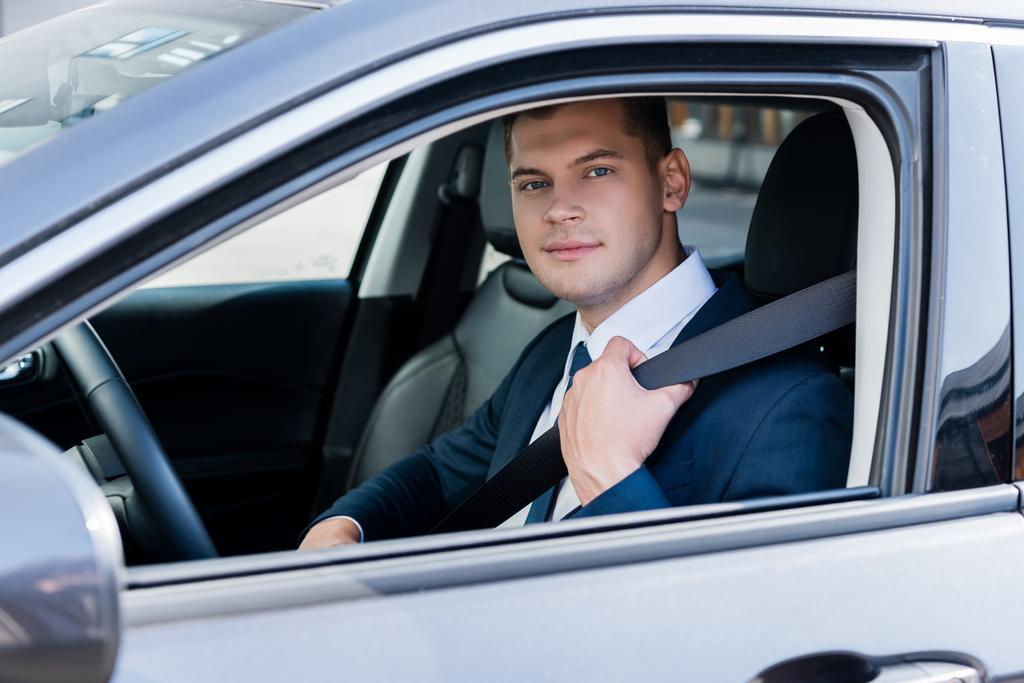 Бизнесмен в формальной одежде держит ремень безопасности в машине и смотрит в камеру - Фото, изображение