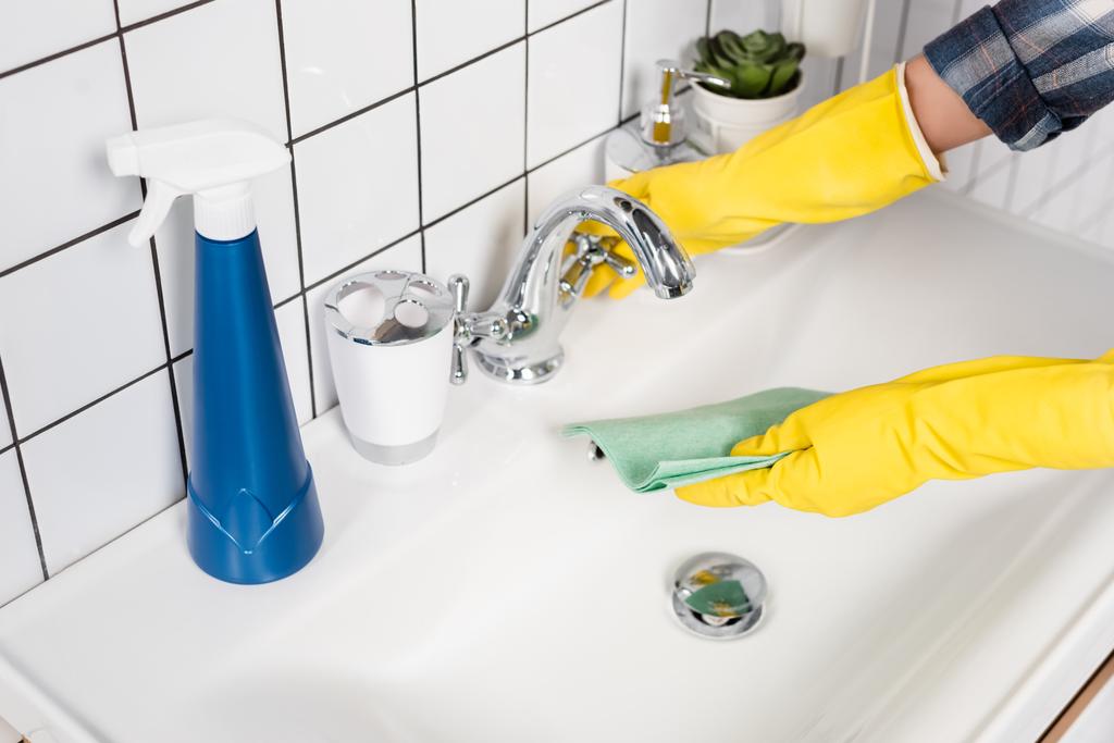 Gewassen uitzicht van de vrouw in rubber handschoenen bevochtigen doek in de buurt wasmiddel op wastafel in de badkamer  - Foto, afbeelding