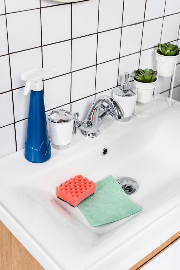 Mosószer palack szivacs és rongy közelében a mosogatóban a modern fürdőszobában  - Fotó, kép
