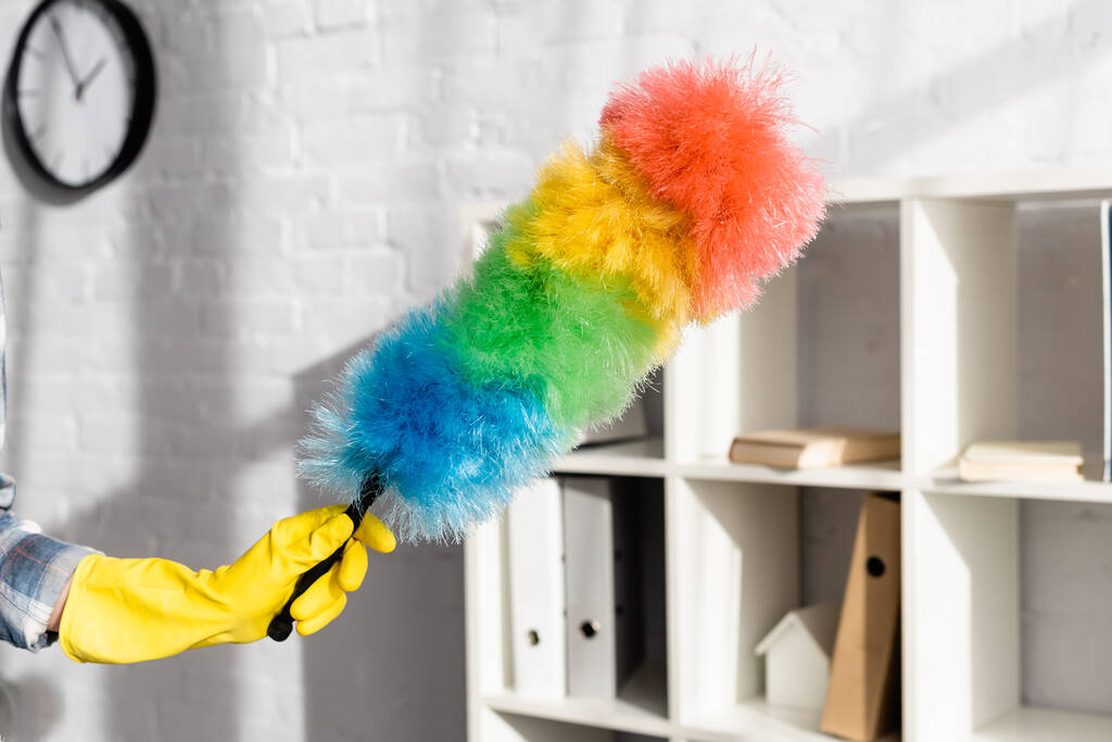 Vista recortada de la mujer en guante de goma amarillo con cepillo de polvo colorido en casa  - Foto, imagen