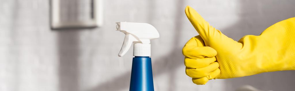 Vista recortada de la persona en guante de goma que muestra como gesto cerca de detergente con rociador, pancarta  - Foto, Imagen