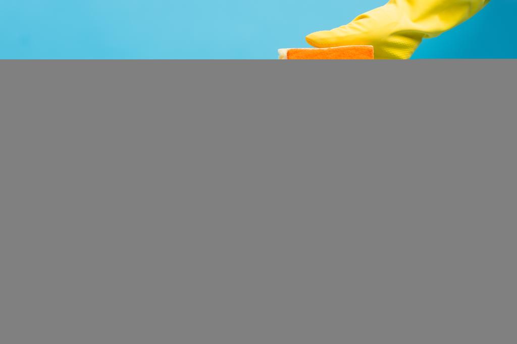Gewassen weergave van persoon in gele rubberen handschoen met spons in de buurt van sponzen op blauwe achtergrond - Foto, afbeelding