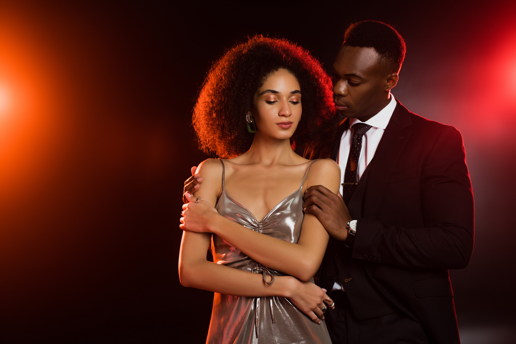 african american man in suit embracing curly woman in dress on black - Photo, Image
