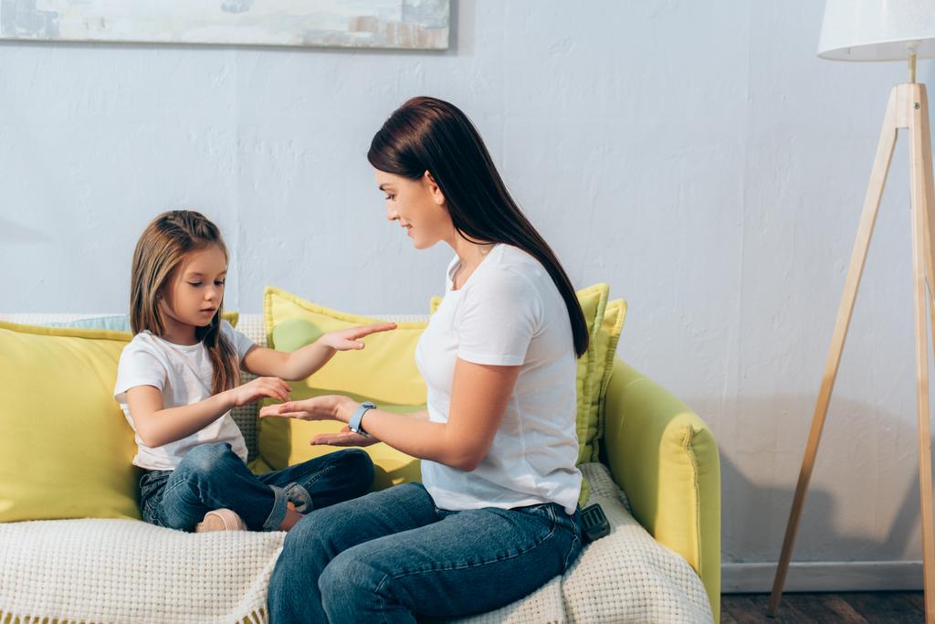 Tochter mit gekreuzten Beinen spielt mit Mutter auf Couch - Foto, Bild
