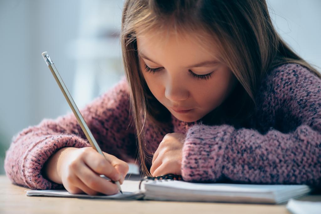Girl with pencil writing in notebook on blurred background - Photo, Image