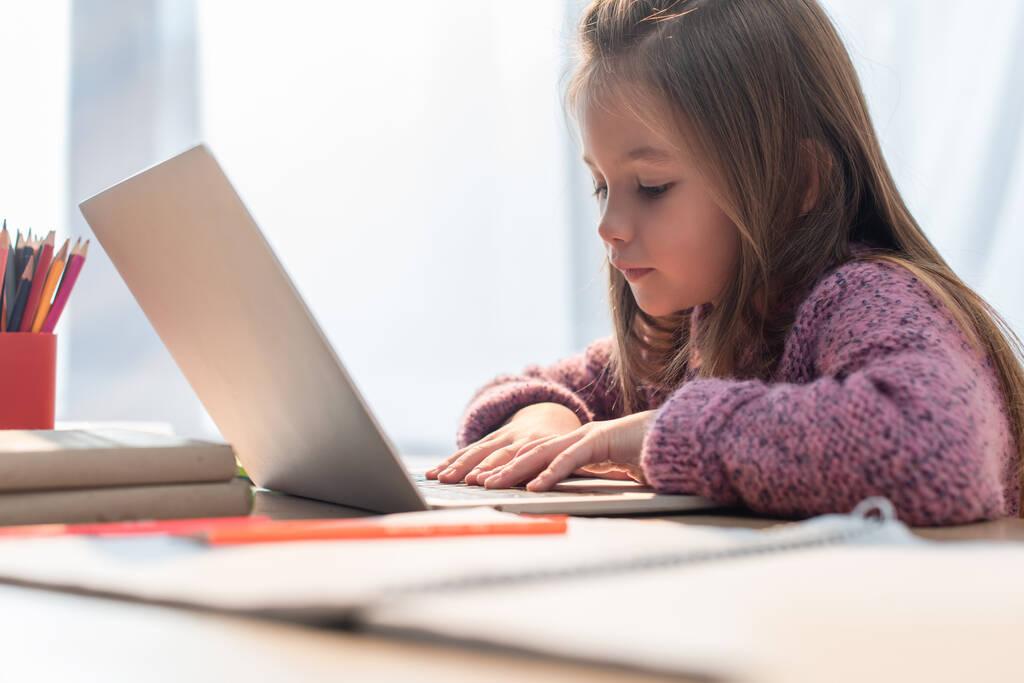 Chica escribiendo en el ordenador portátil en el escritorio en primer plano borrosa - Foto, Imagen