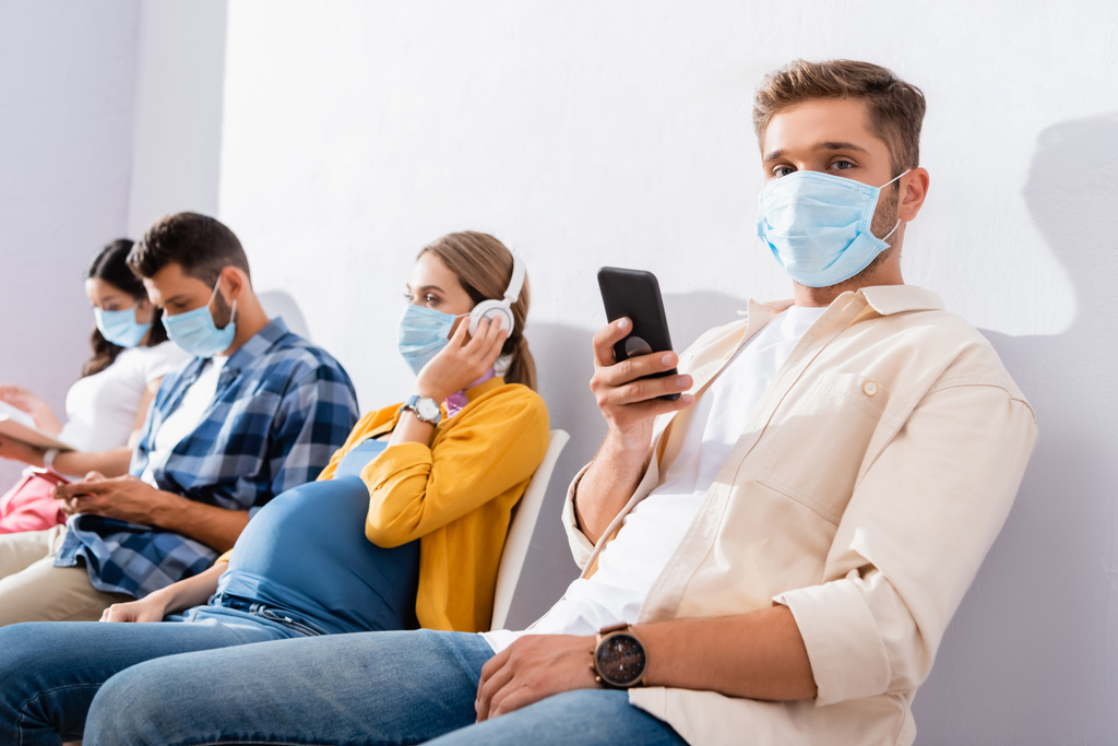 Man met medisch masker houden smartphone in de buurt van zwangere vrouw in de wachtrij  - Foto, afbeelding