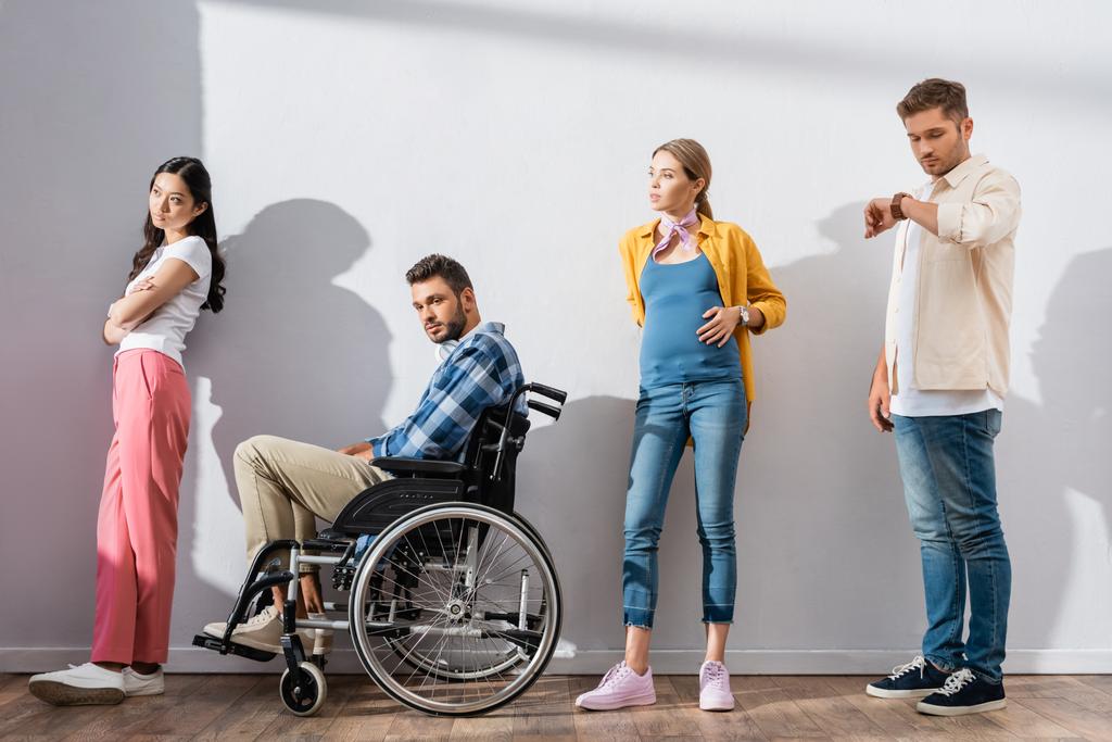 Wieloetniczni ludzie i niepełnosprawny stojący obok ściany w kolejce  - Zdjęcie, obraz