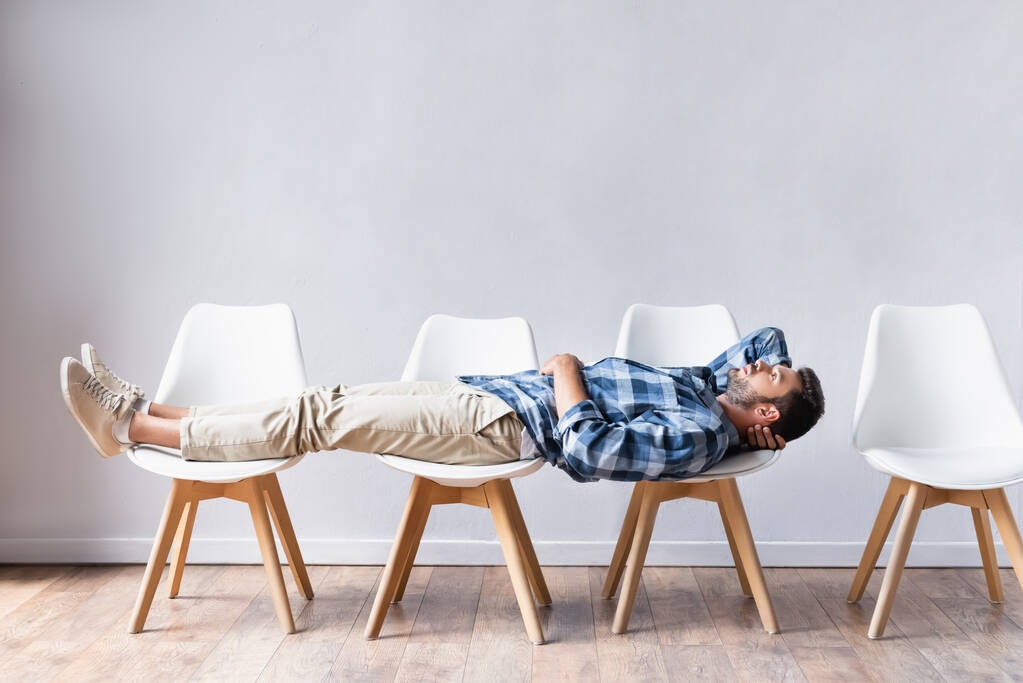 Чоловік в повсякденному одязі лежить на стільцях, чекаючи в залі
  - Фото, зображення