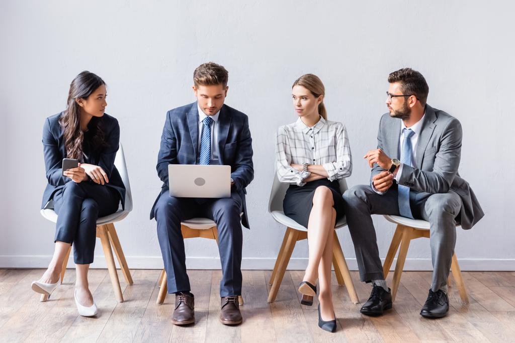 Empresários multiétnicos olhando para homem de negócios com laptop antes da entrevista de emprego no escritório  - Foto, Imagem