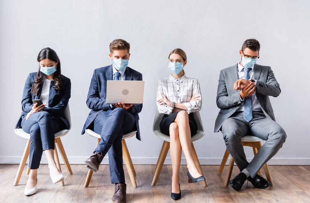 Wieloetniczni biznesmeni w maskach medycznych korzystający z urządzeń przed rozmową kwalifikacyjną  - Zdjęcie, obraz