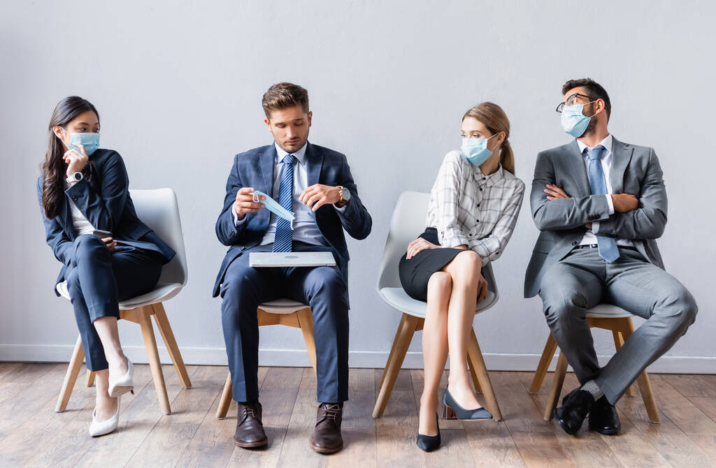Multicultural business people in medical masks looking at man with laptop in hall  - Photo, Image