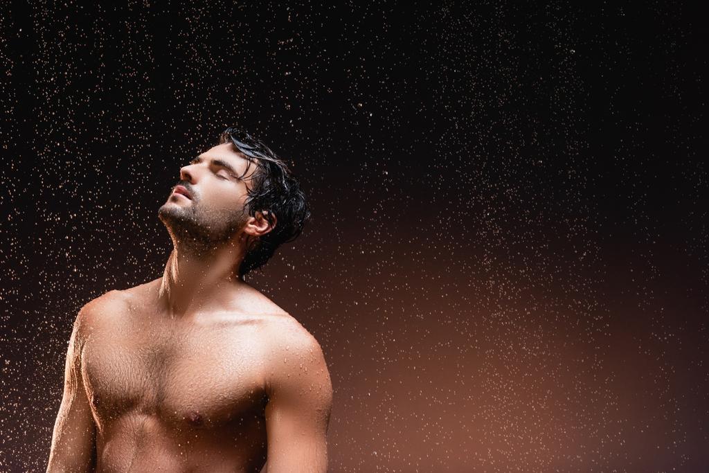 Gövdesi kaslı üstsüz bir adam yağmurun altında karanlık arka planda duruyor. - Fotoğraf, Görsel