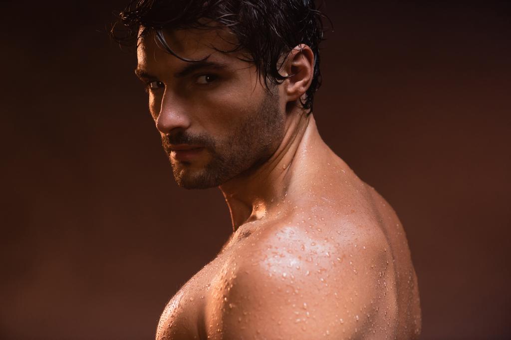 mokry, sexy mężczyzna patrząc w aparat podczas pozowania na ciemnym tle - Zdjęcie, obraz
