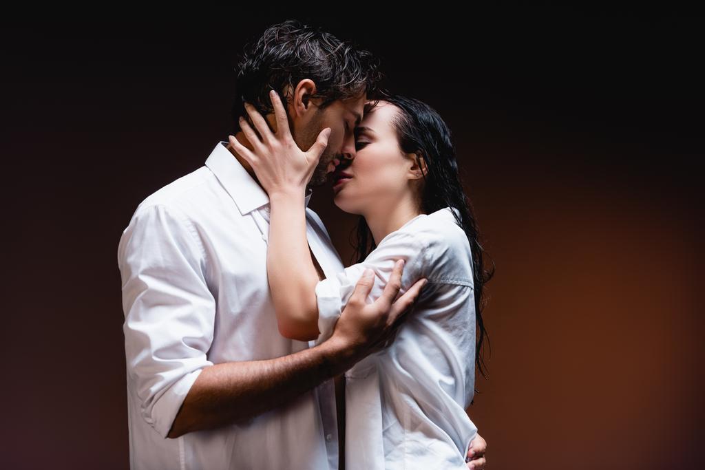 giovane coppia in camicie bianche bagnate abbracciare e baciare su sfondo scuro - Foto, immagini