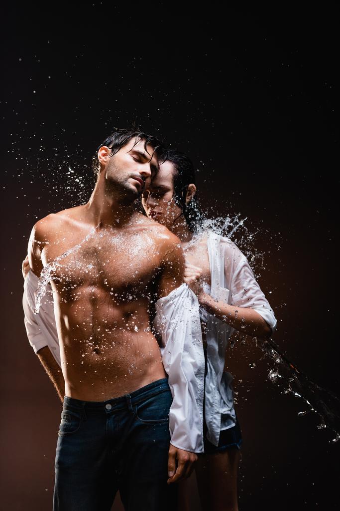 junge Frau zieht sich sexy aus, muskulöser Mann in Wassernähe spritzt auf dunklem Hintergrund - Foto, Bild