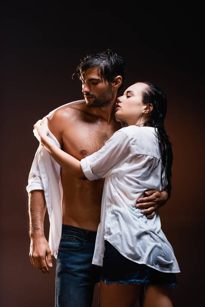 соблазнительная женщина снимает мокрую рубашку с сексуального мужчины на темном фоне - Фото, изображение