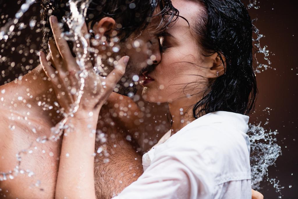 femme embrasser homme torse nu près des éclaboussures d'eau sur fond sombre - Photo, image