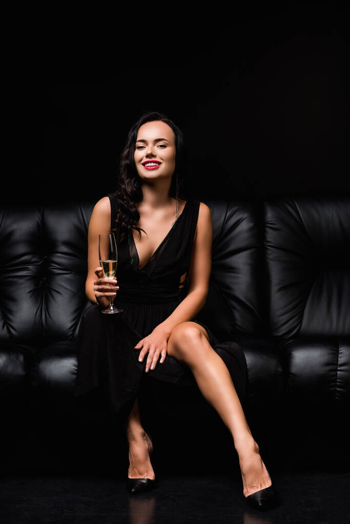 весела жінка в одязі сидить на дивані і тримає келих шампанського на чорному
 - Фото, зображення