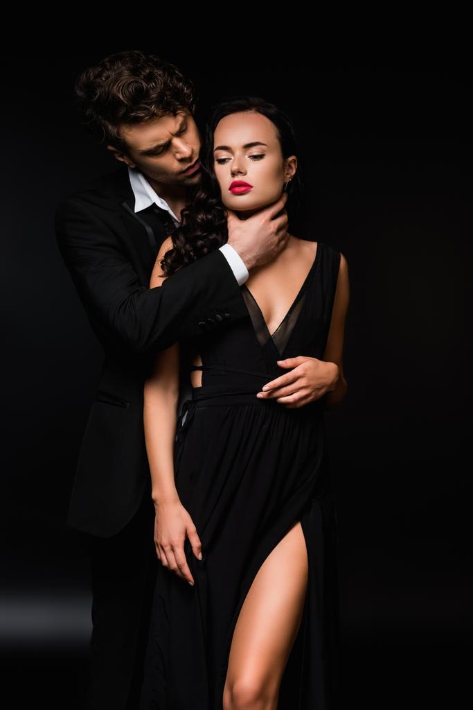 hartstochtelijke man stikken sexy en onderdanig vrouw in jurk op zwart  - Foto, afbeelding
