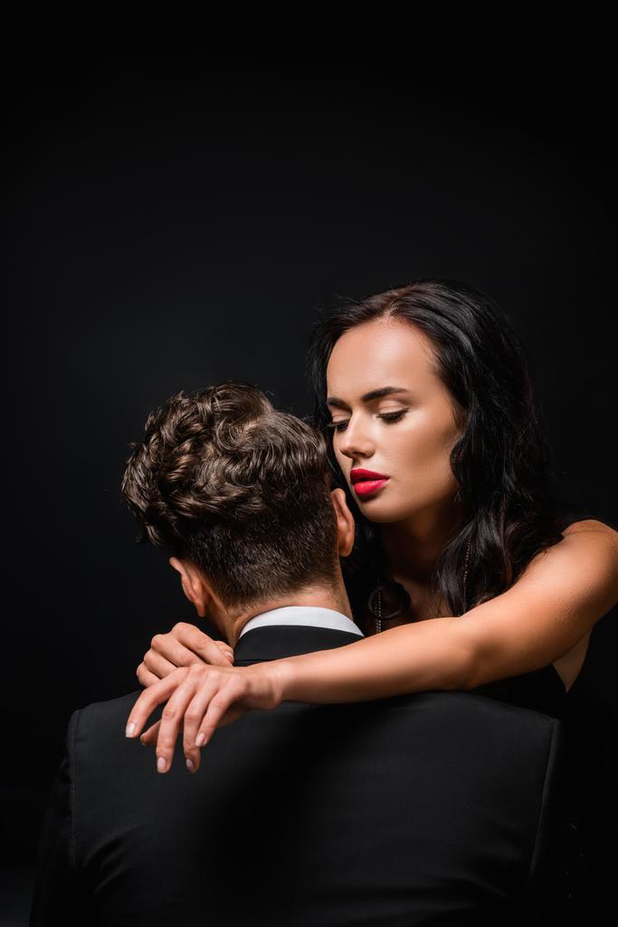 seductive woman with red lips hugging man in suit isolated on black  - Photo, Image