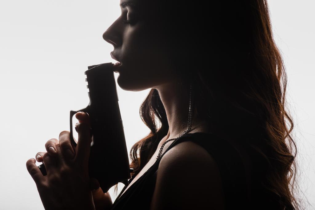 boční pohled na brunetky mladá žena se zavřenýma očima držení zbraň izolované na bílém - Fotografie, Obrázek