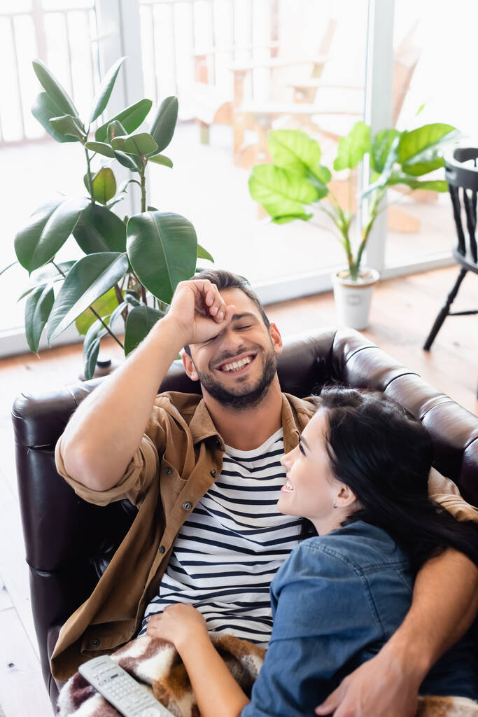 fröhlicher Mann lacht mit geschlossenen Augen, während er mit Freundin auf Ledercouch ruht - Foto, Bild