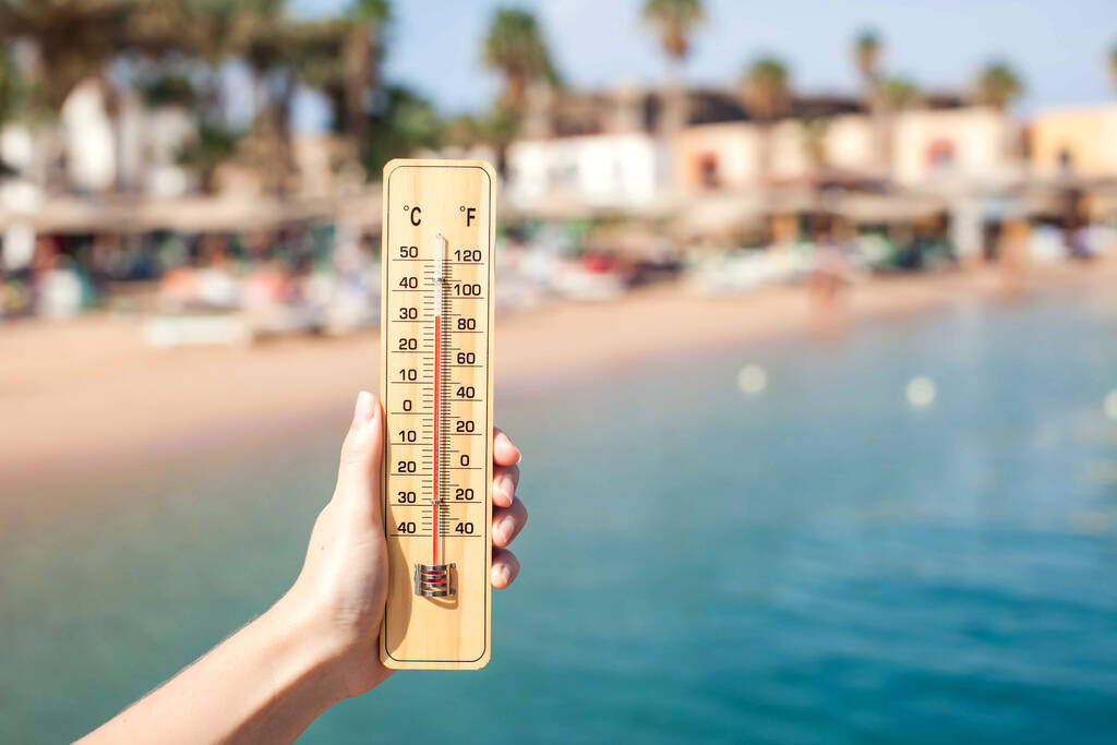 女性の手はビーチの背景に温度計を保持します。夏、気候、天候の概念 - 写真・画像