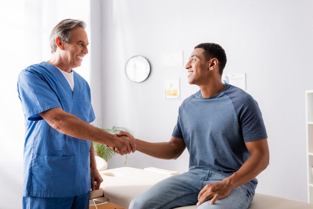 chiropratico felice che stringe la mano al paziente afroamericano  - Foto, immagini