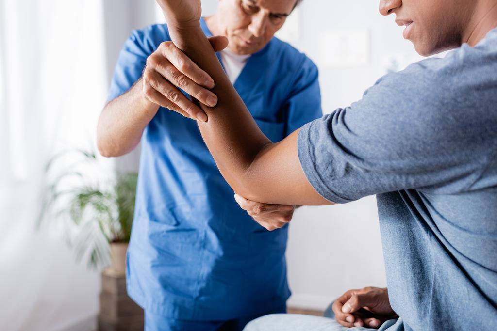kiropraktikko työskentelee afrikkalaisen amerikkalaisen miehen loukkaantuneen käden kanssa klinikalla - Valokuva, kuva