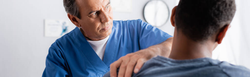 kiropraktikko työskentelee afrikkalaisen amerikkalaisen miehen loukkaantuneen käden kanssa hämärtyneessä etualalla, bannerissa  - Valokuva, kuva