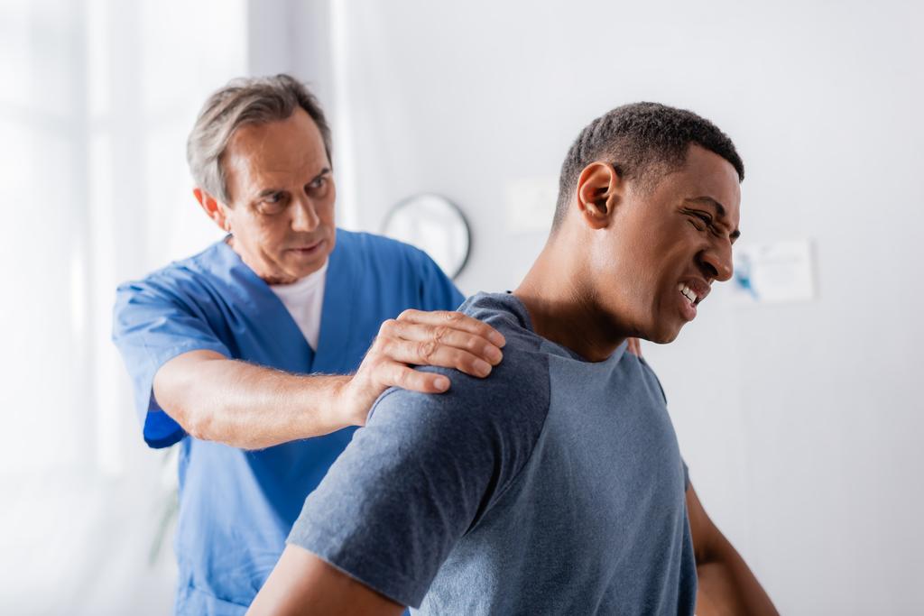 Klinikte acı çeken yaralı Afrikalı Amerikalı bir adamla çalışan bir doktor. - Fotoğraf, Görsel