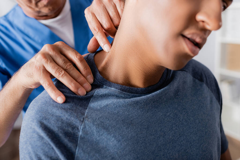 przycięty widok masażysty masujący rannego amerykańskiego pacjenta w klinice  - Zdjęcie, obraz