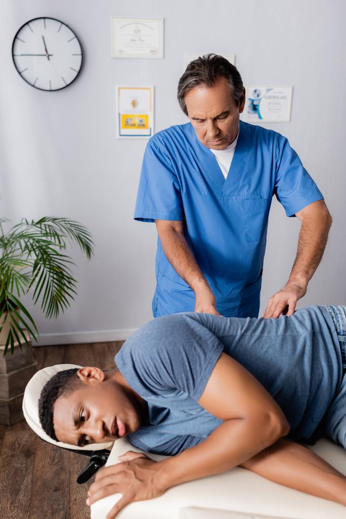 Chiropraktiker mittleren Alters arbeitet mit afrikanisch-amerikanischen Patienten auf Massagetisch - Foto, Bild