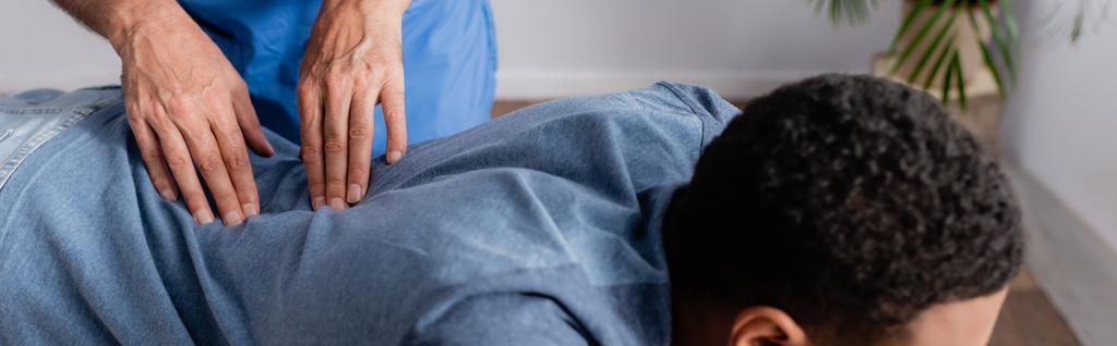 částečný pohled na chiropraktika při práci s mladým afroamerickým pacientem na klinice, banner - Fotografie, Obrázek