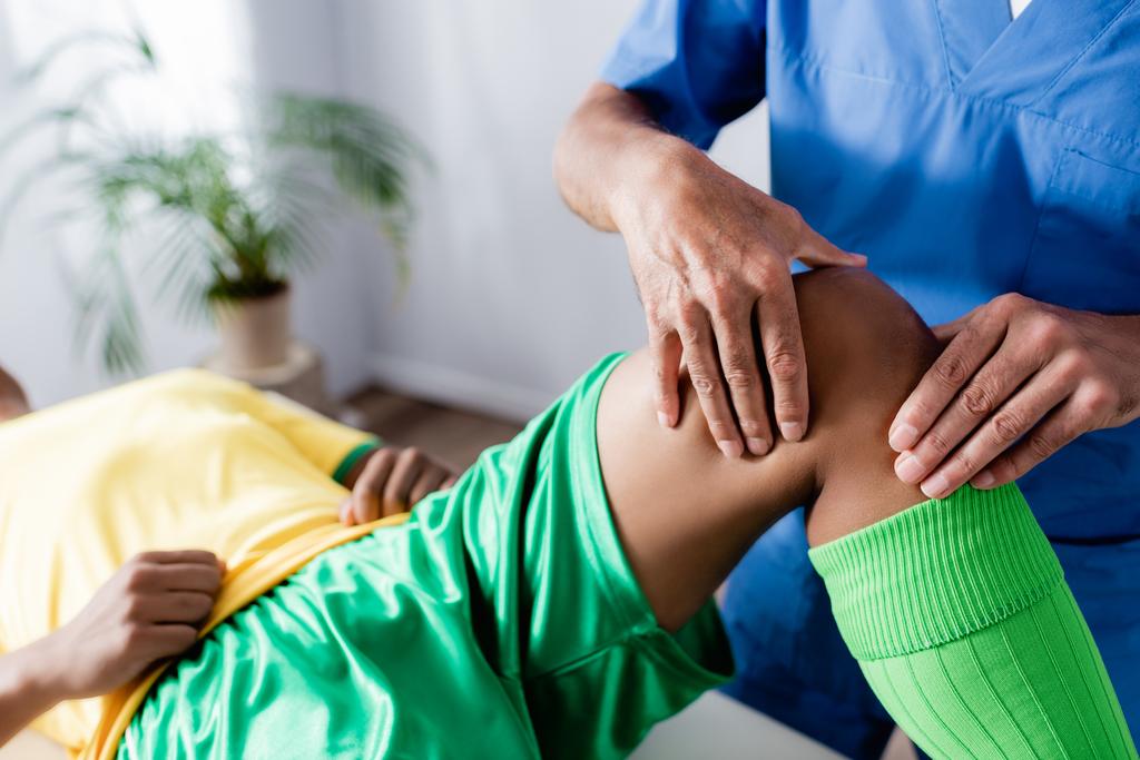 vista ritagliata di massaggiatore massaggio ginocchio di sportsman africano americano - Foto, immagini