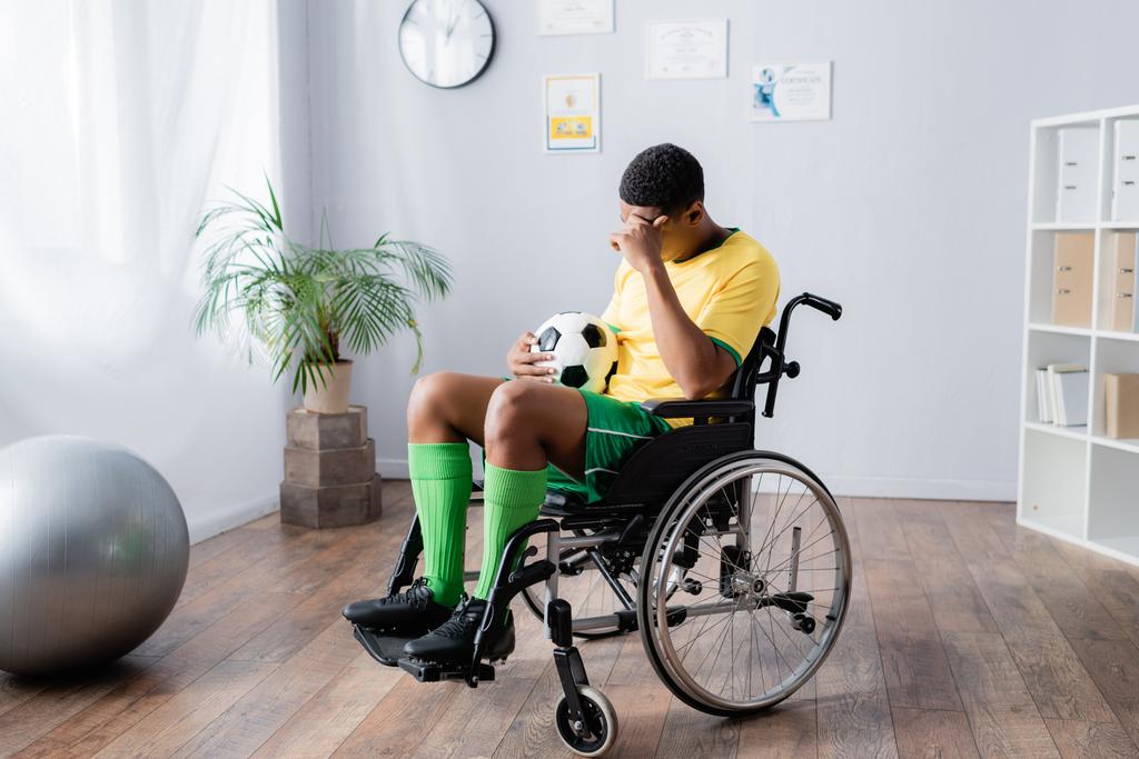 αναστατωμένος άτομα με ειδικές ανάγκες Αφροαμερικανός αθλητής σε αναπηρικό αμαξίδιο κρατώντας το ποδόσφαιρο  - Φωτογραφία, εικόνα