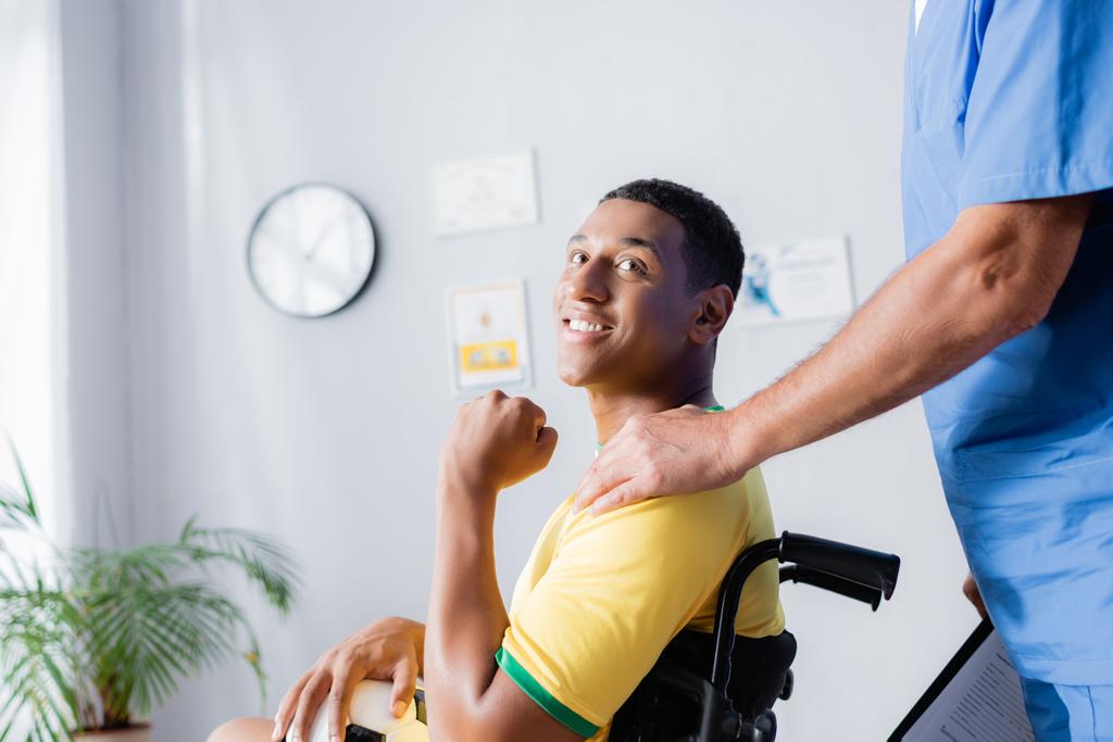 zralé lékař dotýká rameno veselého zdravotně postiženého sportovce na klinice  - Fotografie, Obrázek