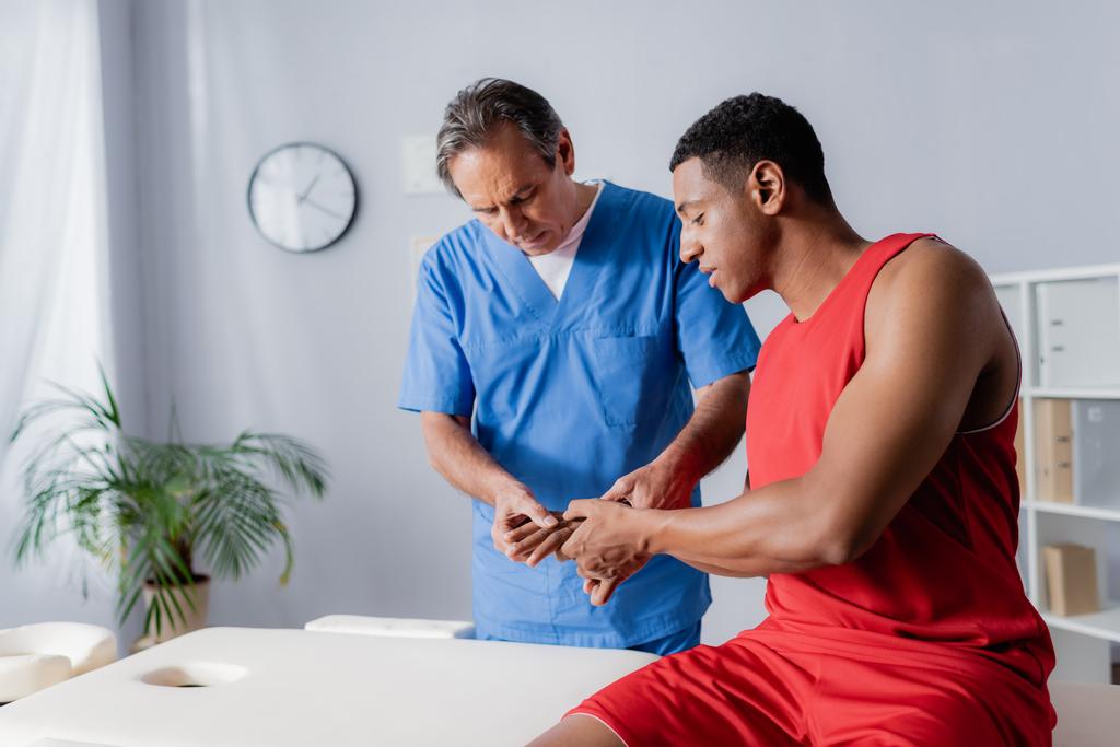 chiropraticien d'âge moyen travaillant avec un homme afro-américain en vêtements de sport  - Photo, image