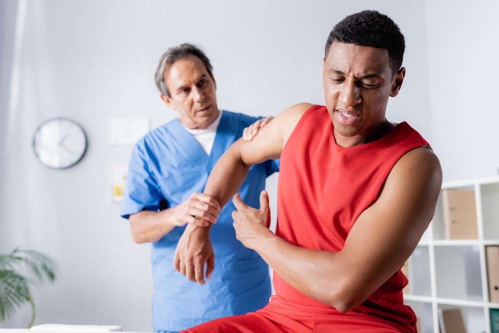 mature chiropractor working with injured african american man in sportswear  - Photo, Image
