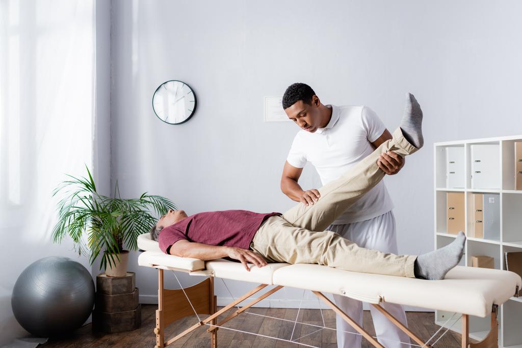 africký americký chiropraktik pracující s mužem středního věku na moderní klinice - Fotografie, Obrázek