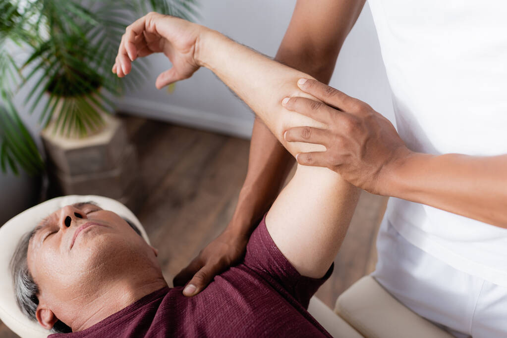 africký americký chiropraktik opravující ruku člověka na masážním stole - Fotografie, Obrázek