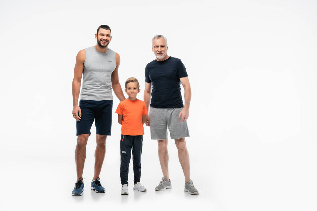 heureux garçon avec papa et grand-père en vêtements de sport en regardant la caméra sur blanc - Photo, image